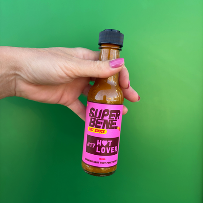 Hand holding a bottle of Super Bene hot sauce against a green background hot lover