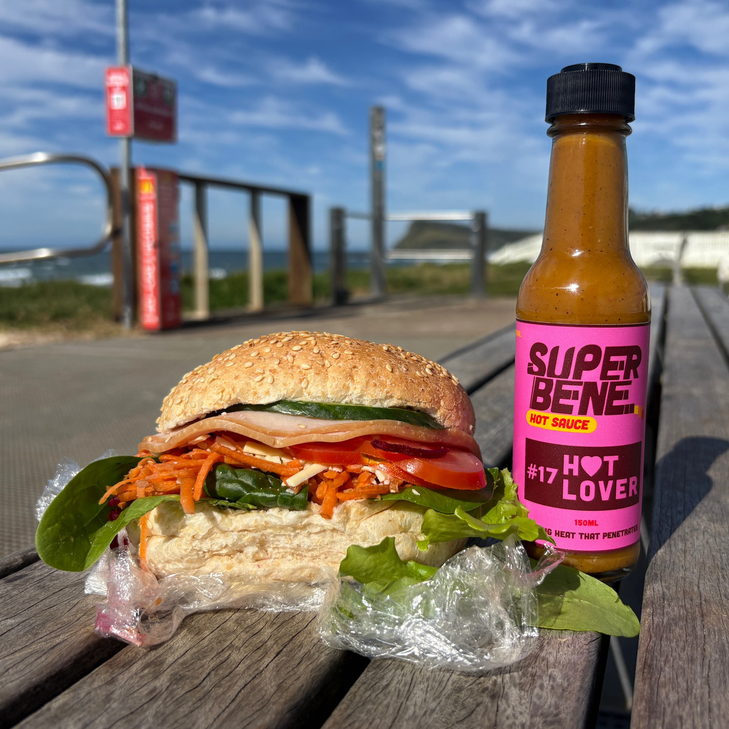 Sandwich with various ingredients on a wooden surface next to a bottle of Super Bene hot sauce.